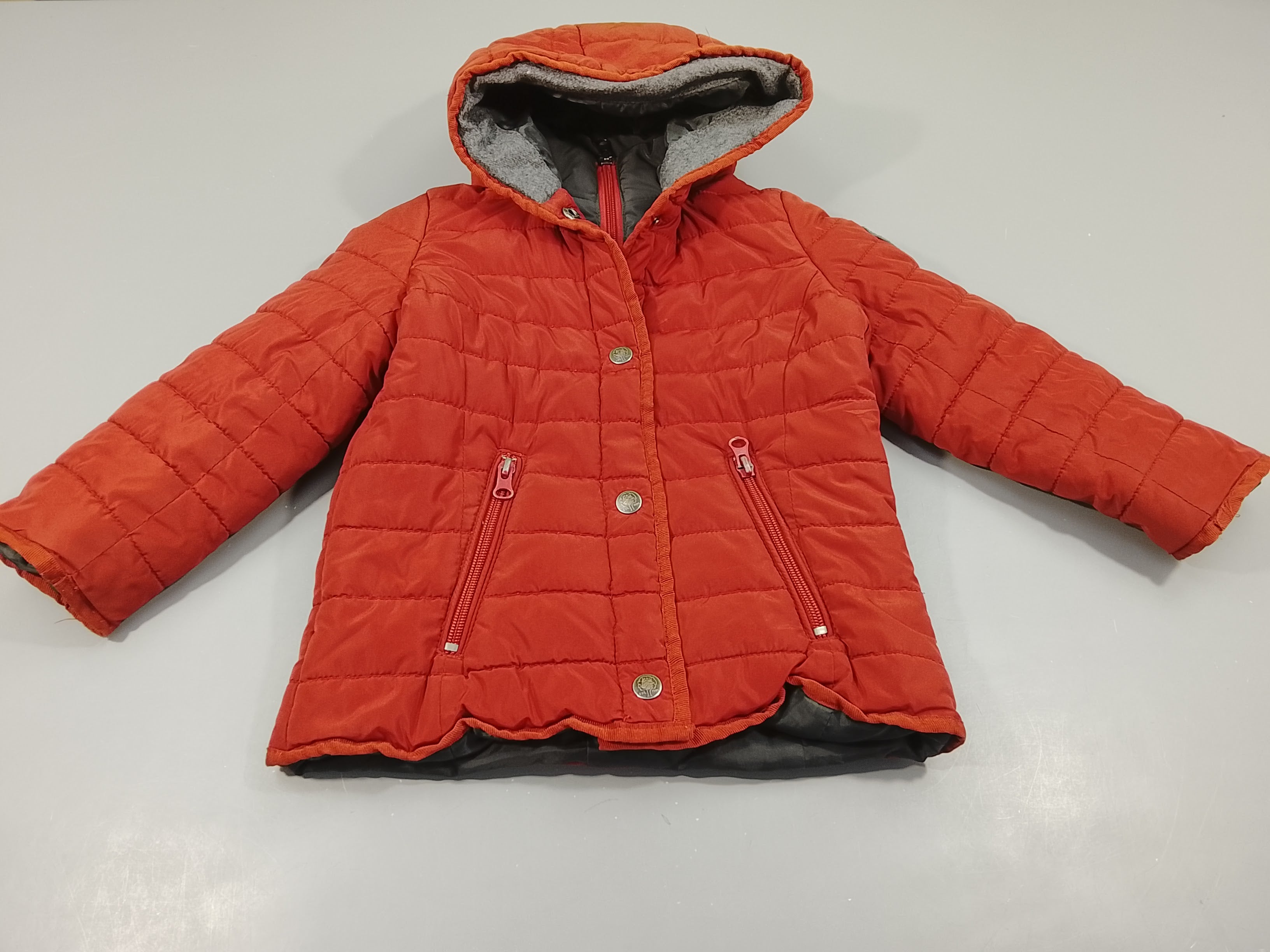 Veste à capuche matelassée rouge brique, double fermeture zip et et pressions, pas de taille indiquée, estimée 6a
