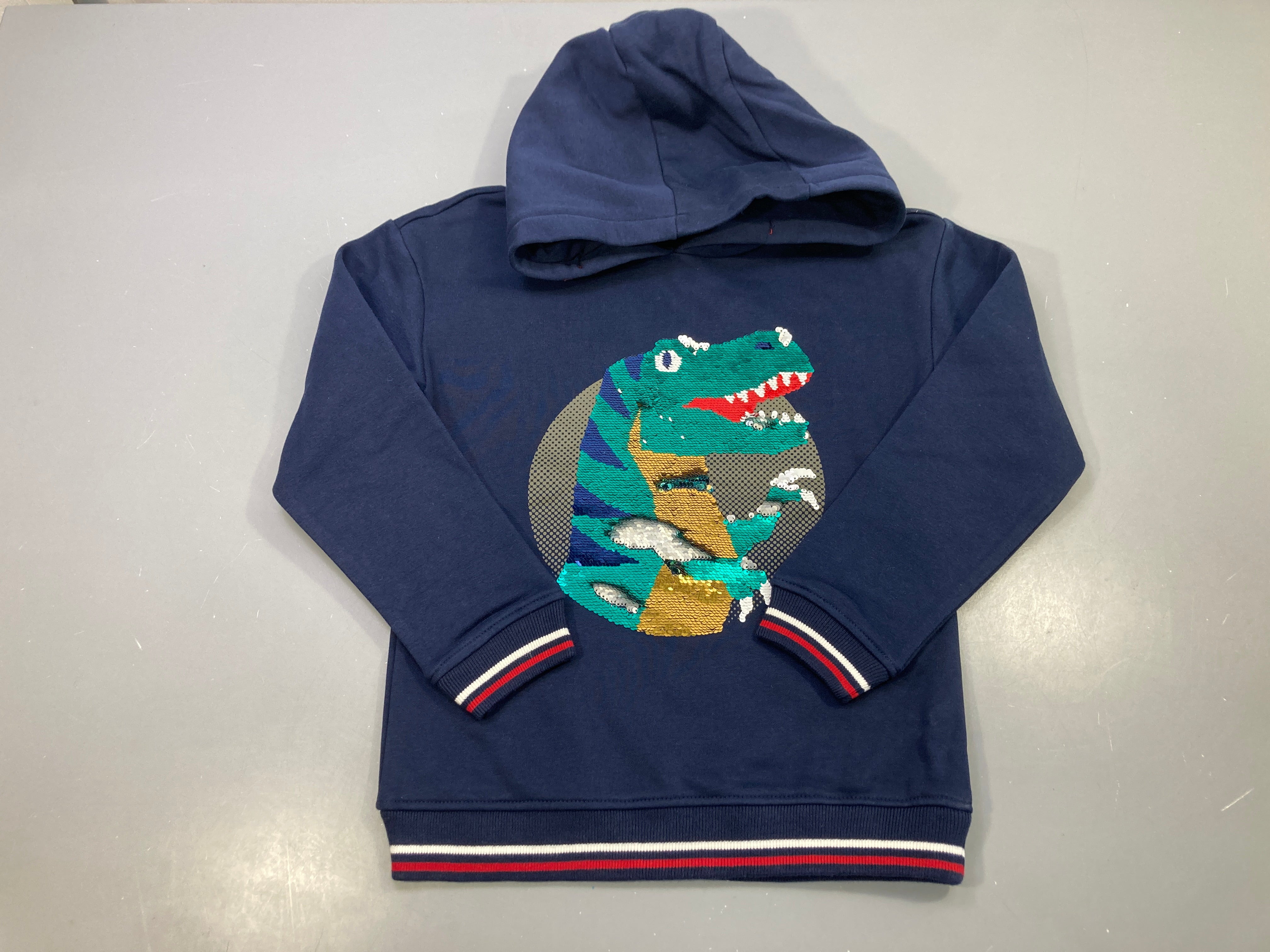 Sweat capuche bleu marine, dinosaure en sequins réversibles, bords rayés rouge et blanc