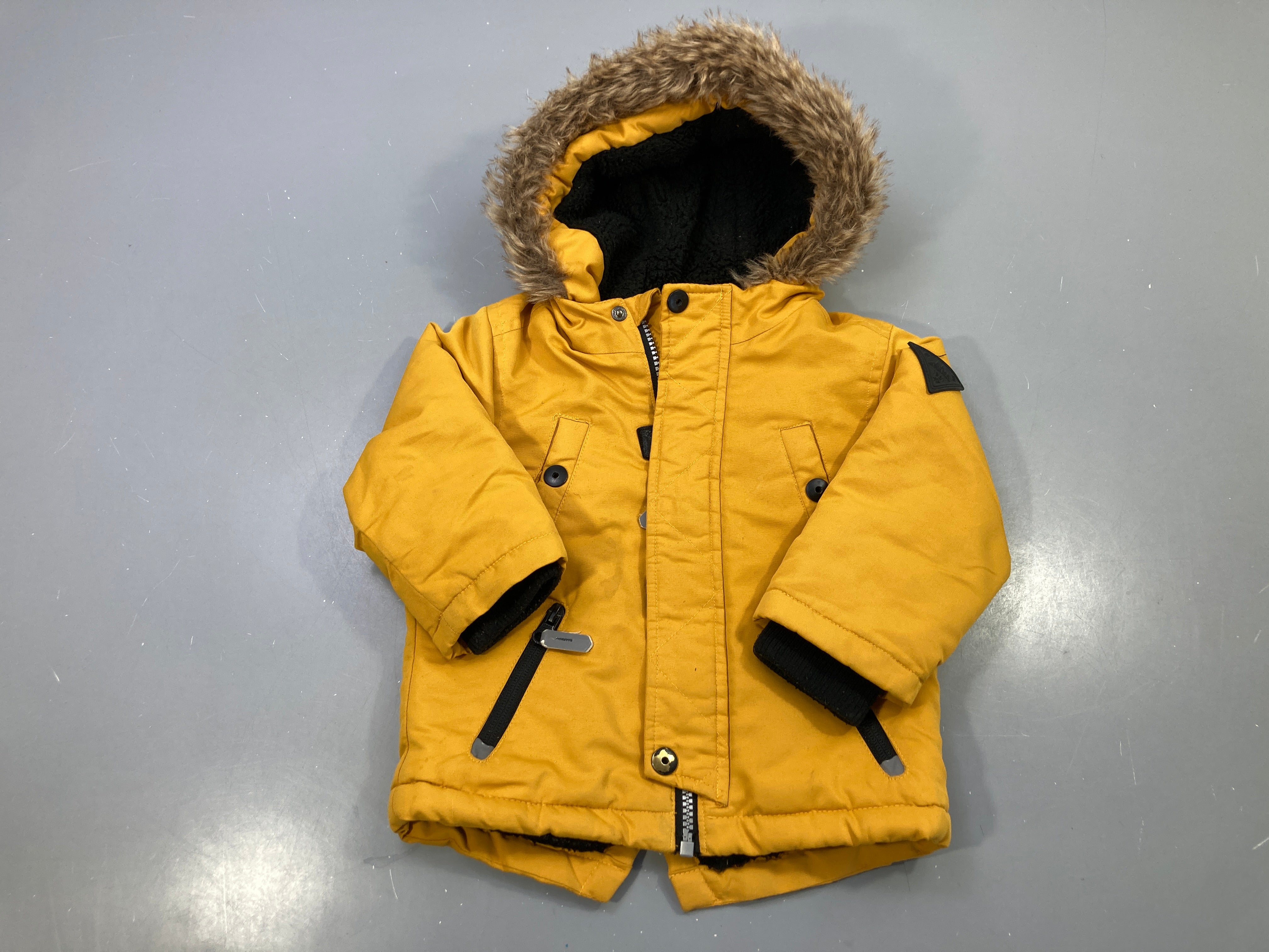 Parka moutarde, capuche fausse fourrure, doublure sherpa noire, zippée, tache à l'avant